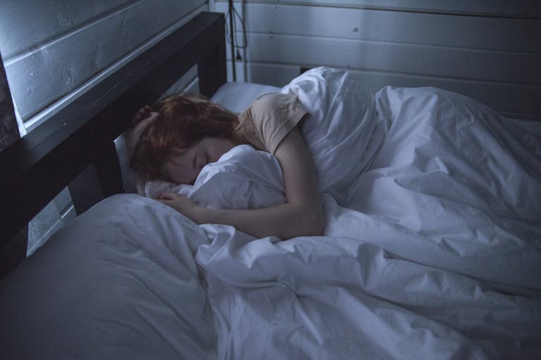 Jovem mulher dormindo profundamente em sua cama, coberta e serena num amanhecer cinza e escuro, momento em que ela sonha com os significados profundos de suas vivências.