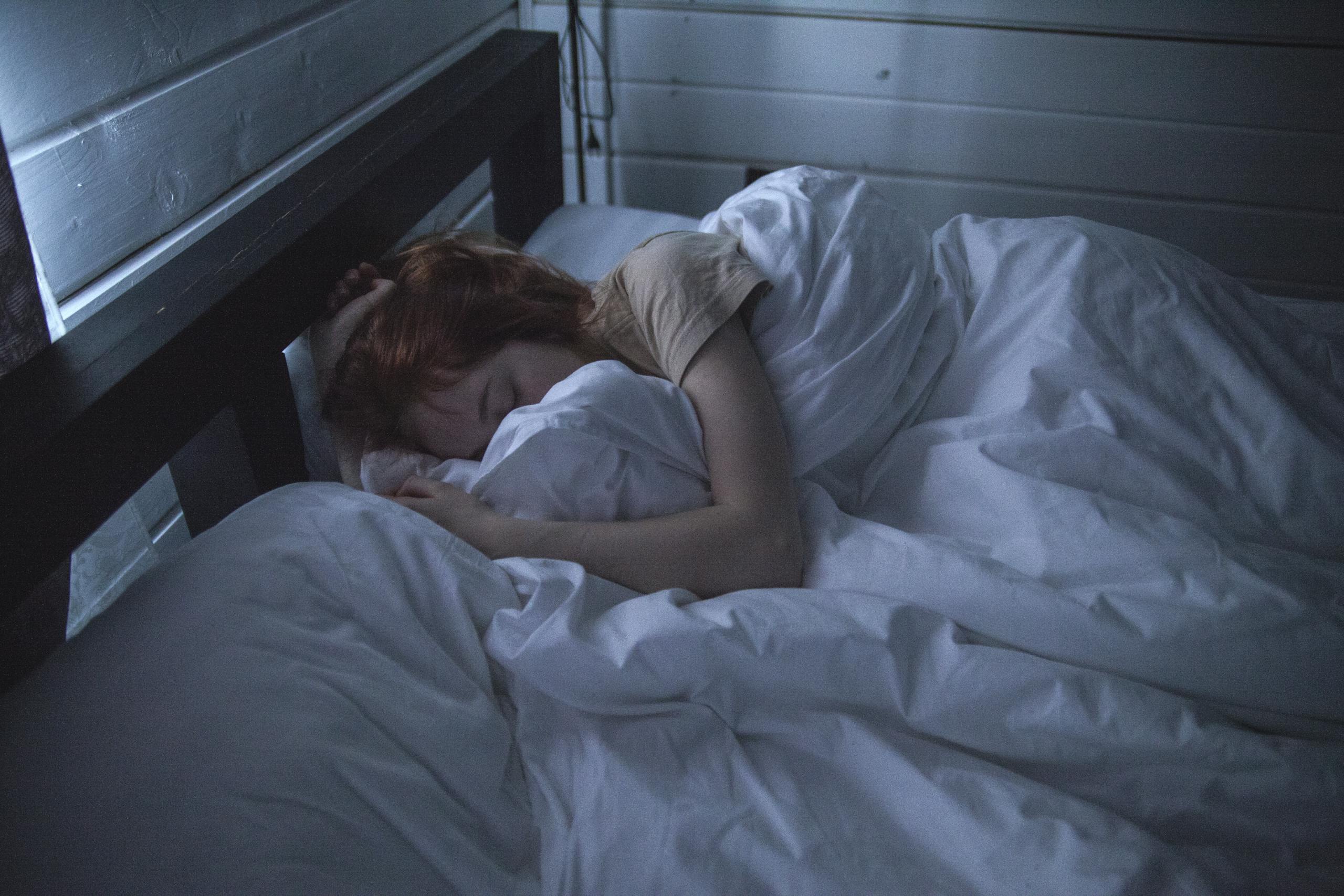 Jovem mulher dormindo profundamente em sua cama, coberta e serena num amanhecer cinza e escuro, momento em que ela sonha com os significados profundos de suas vivências.