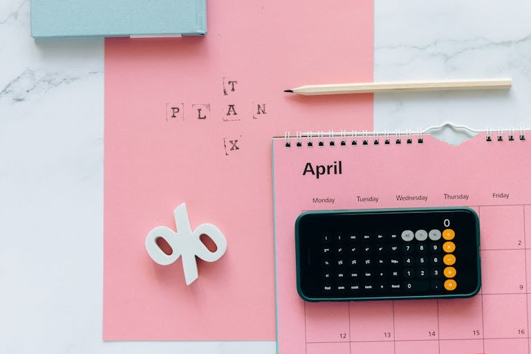Planejamento da Restituição de Imposto de Renda em abril: calendário, calculadora e lápis sobre fundo rosa, representando a organização para a declaração do IRPF.